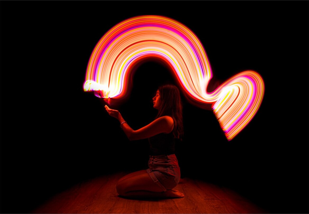 Light painting: una persona de rodillas en la oscuridad dibuja un arco de luz naranja y rosa con una linterna