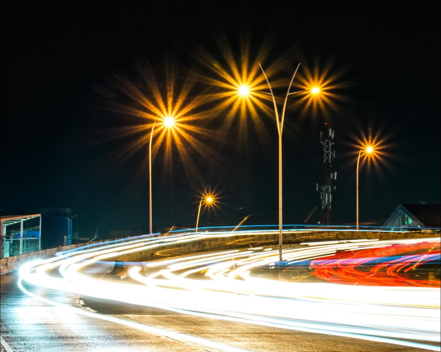 Larga exposición nocturna: las luces de los coches dejan estelas blancas y rojas en una curva, bajo farolas convertidas en estrellas