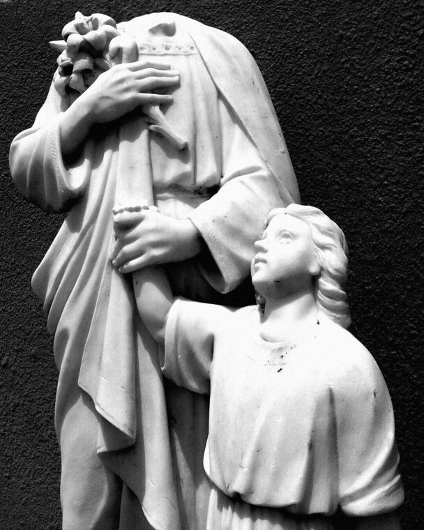 Estatua blanca de una figura abrazando a dos niños, recortada contra una pared oscura. Cabimas.